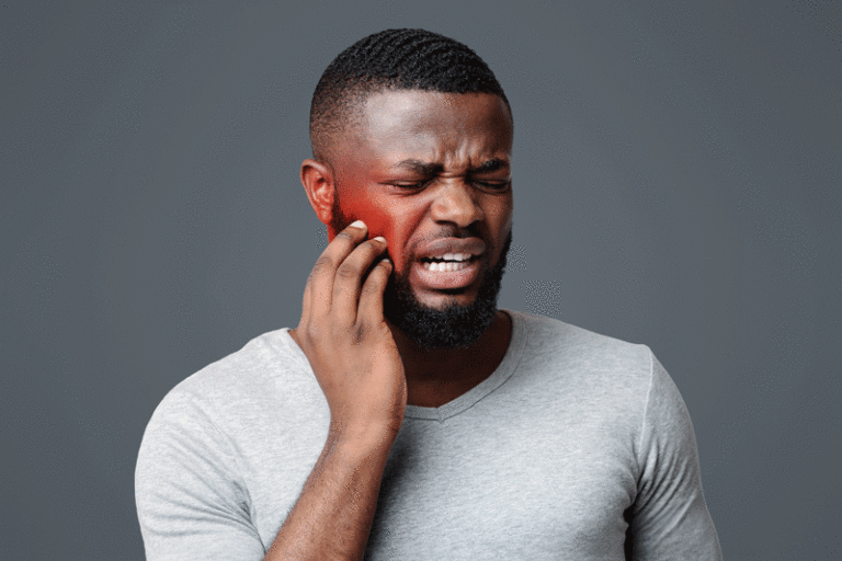 Man in pain touching his cheek, white studio background, tooth disease concept. Grey background, red cheek.